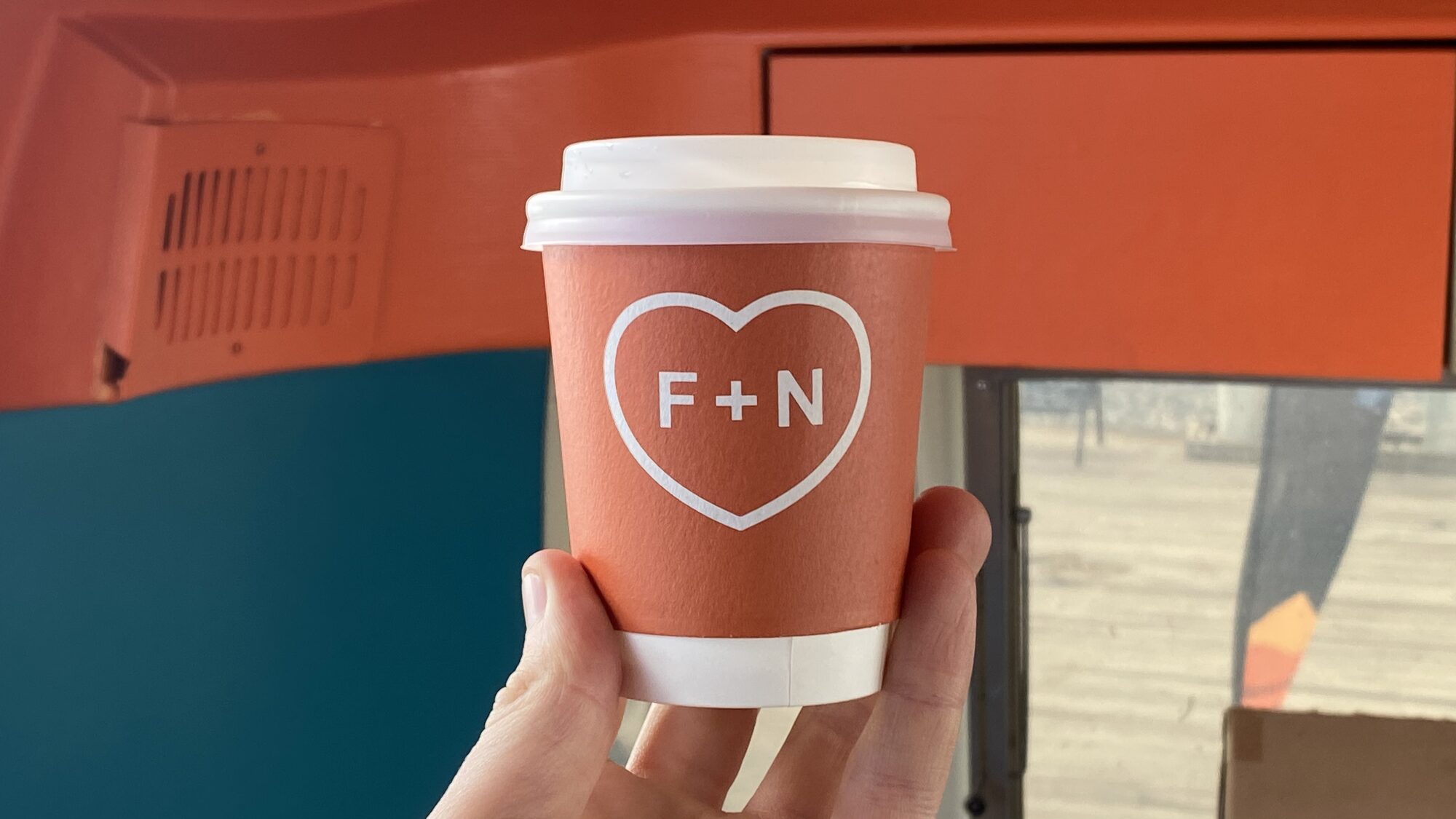 Fred + Nancy's coral takeaway cup with F+N heart mark.