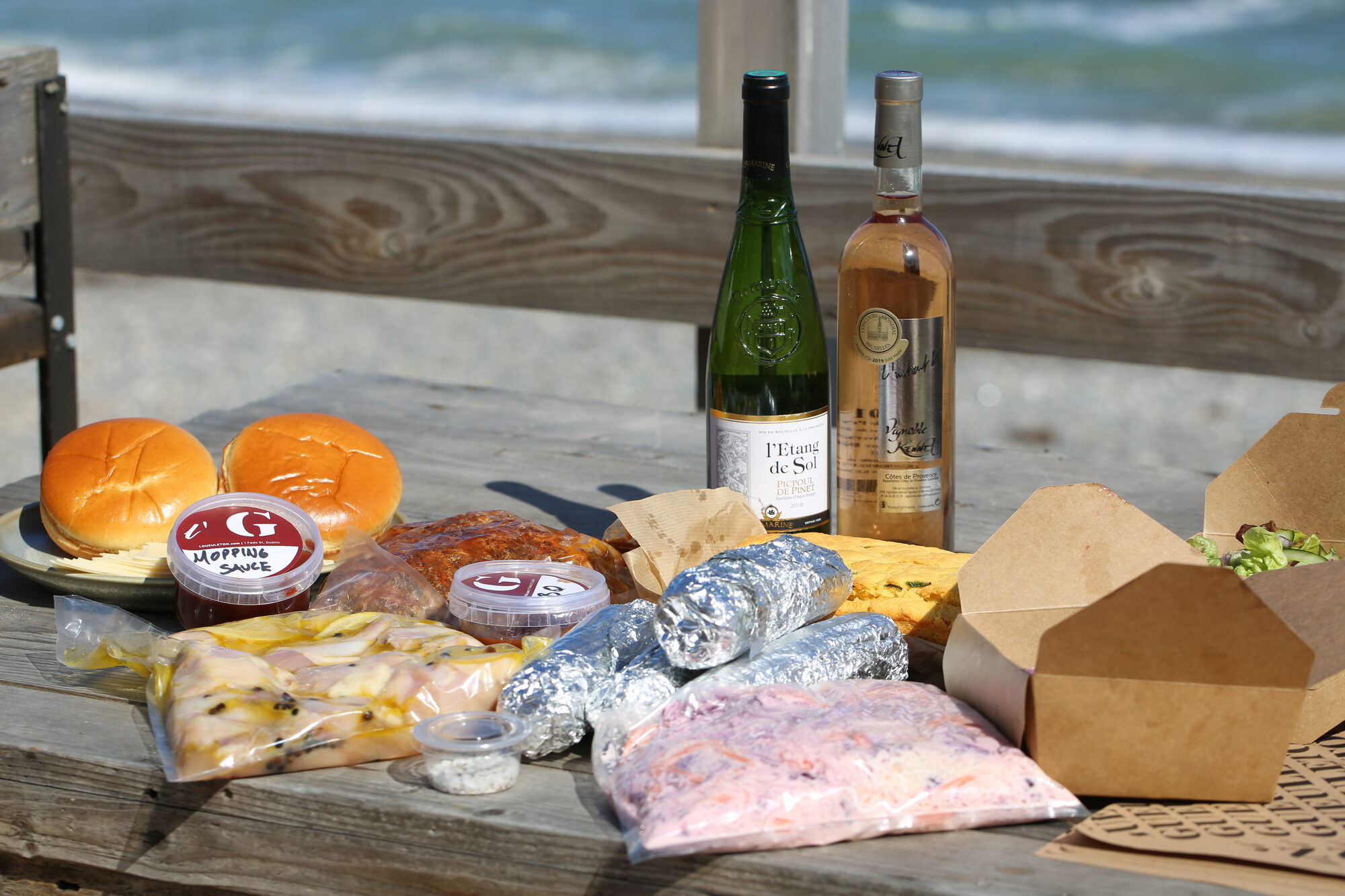 Cook-at-home BBQ spread on the beach with branded materials.