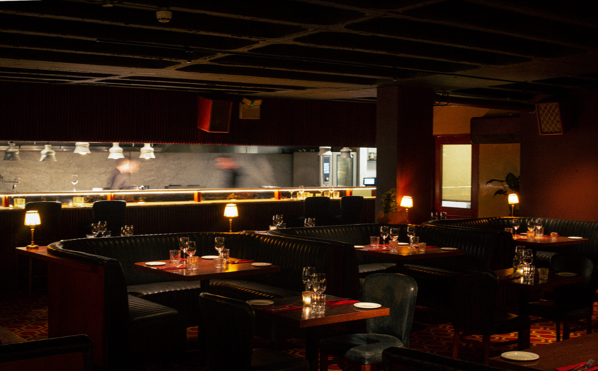 Low-lit Luna dining room with booths, table lamps and an open kitchen in the background.