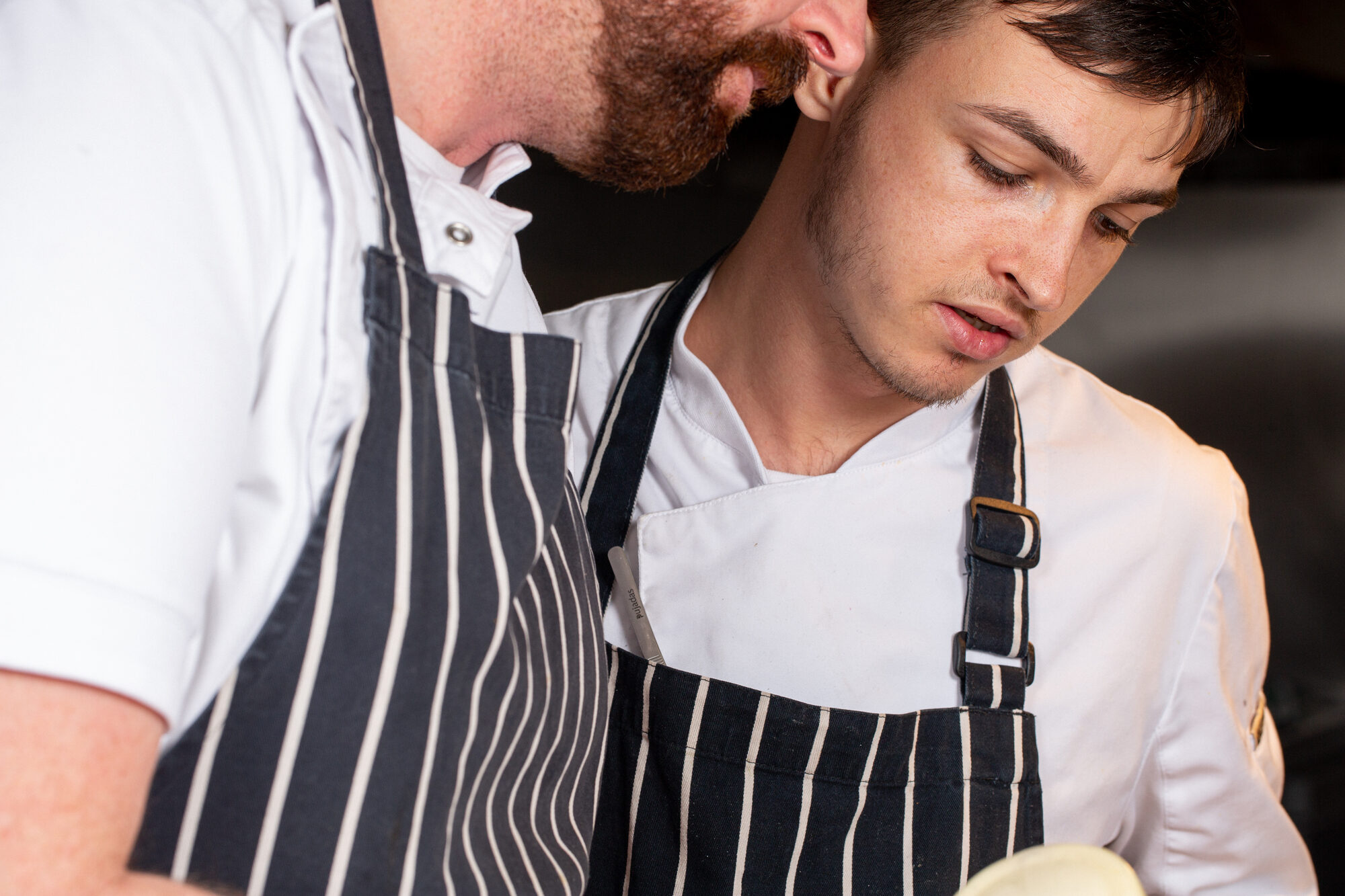 Two chefs in white jackets working closely together in a restaurant kitchen.
