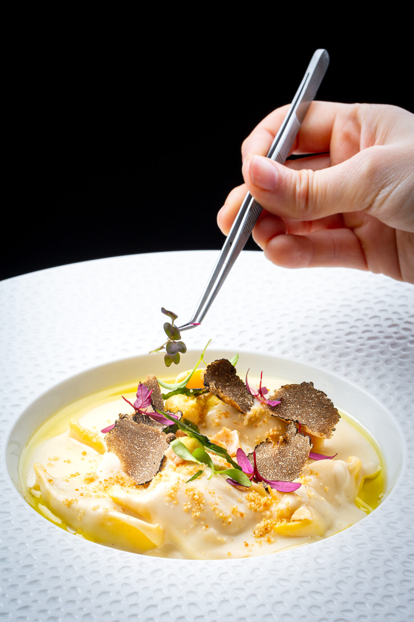 A chef's hand uses tweezers to place a microherb on a dish of truffle tortelloni with cream sauce and microherbs at Luna.
