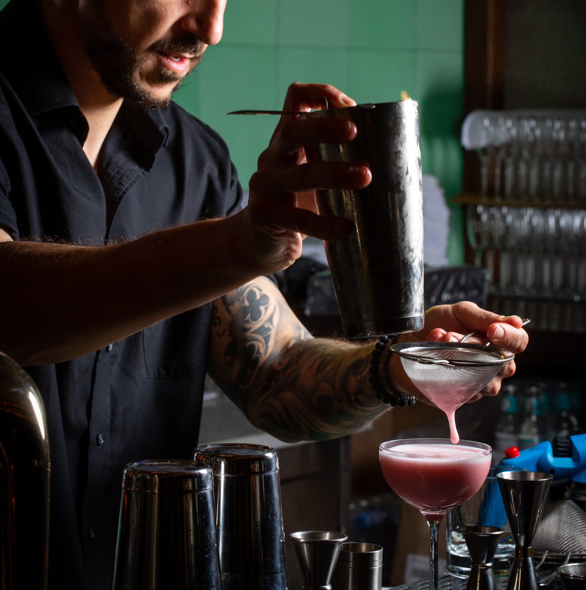 Bartender stirring a drink behind a bar lined with bottles.