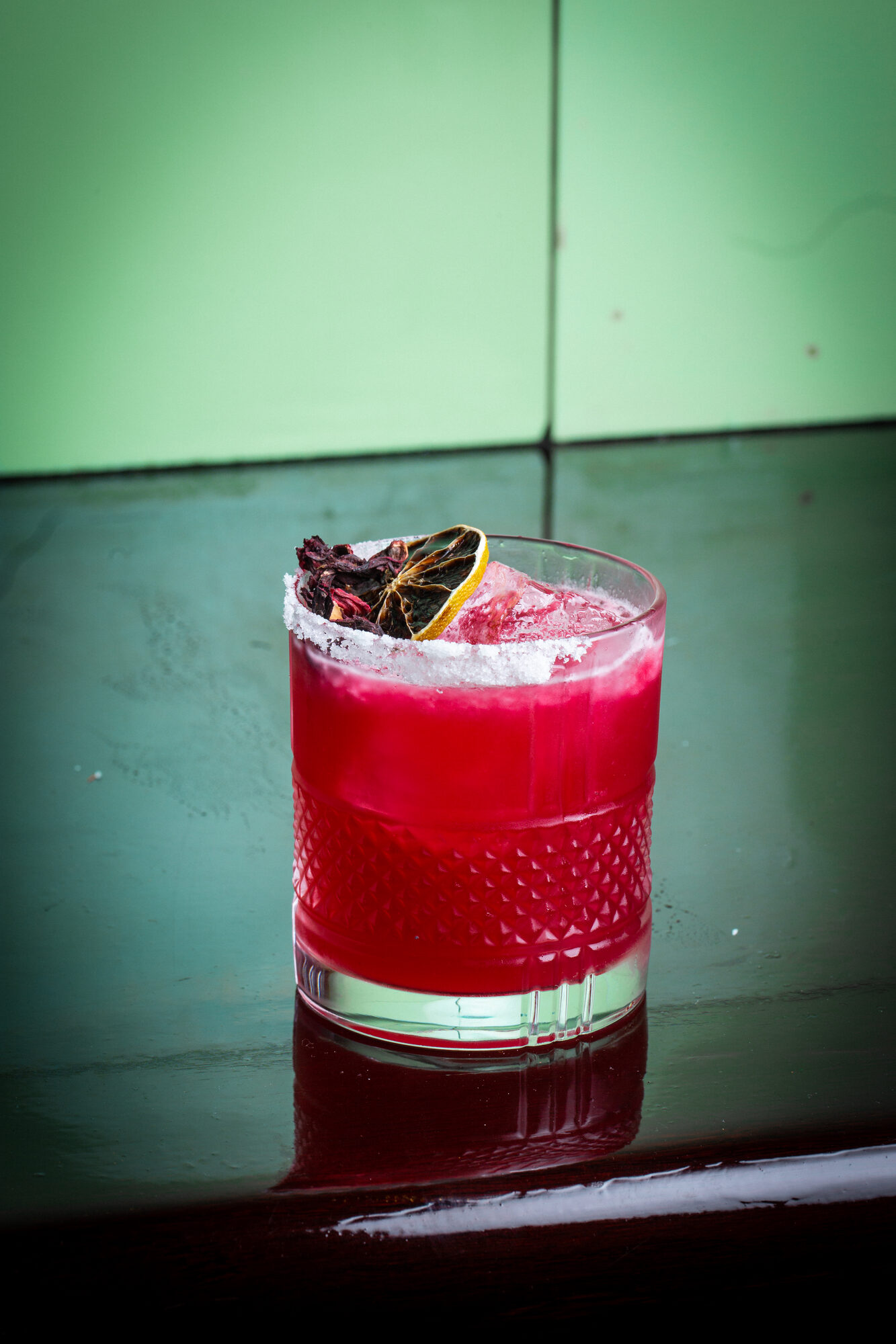 A hibiscus cocktail with garnish, in soft interior light.