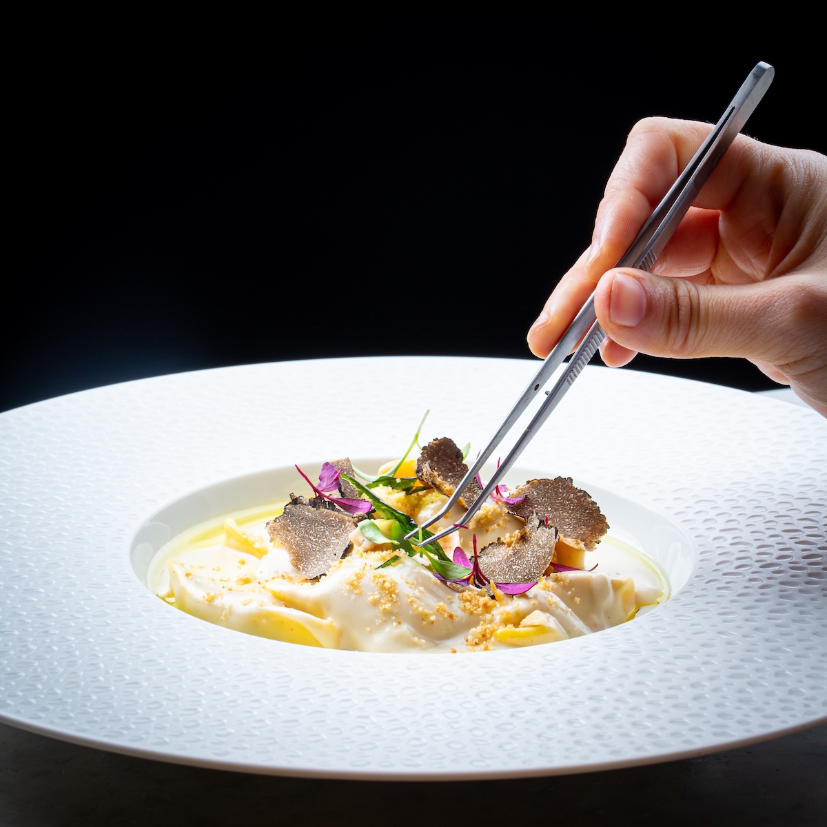 A hand using tweezers to place truffle on a pasta dish — kitchen process from Luna’s reopening shoot.