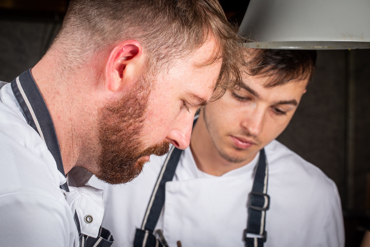 Two chefs in white jackets working closely together in a restaurant kitchen.