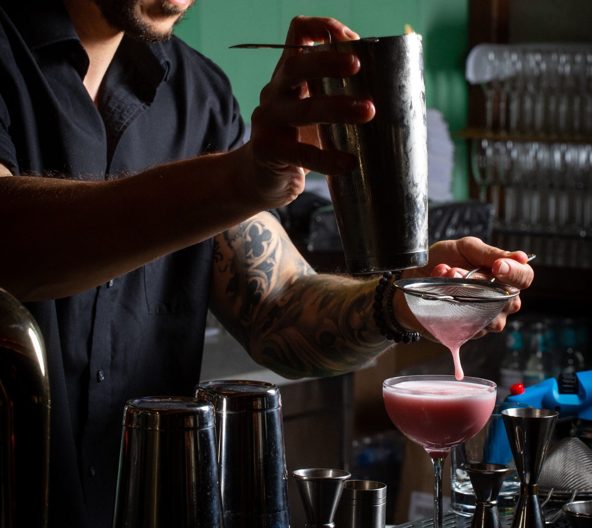 Bartender stirring a drink behind a bar lined with bottles.