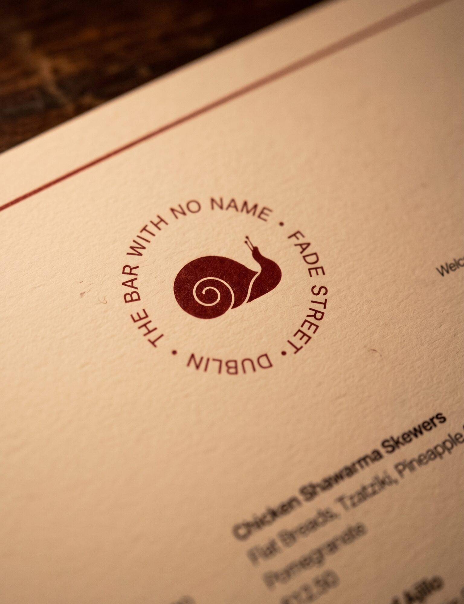 Close-up of the Bar With No Name snail mark printed in oxblood on cream menu paper.