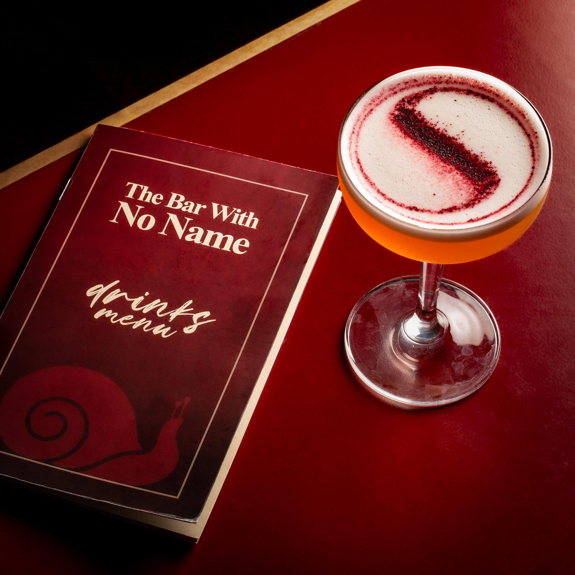 Bar With No Name menu and cocktail on a deep red table.
